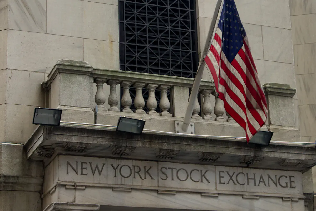 The carved New York Stock Exchange sign on the marble facade on Wall Street, with an American flag above it