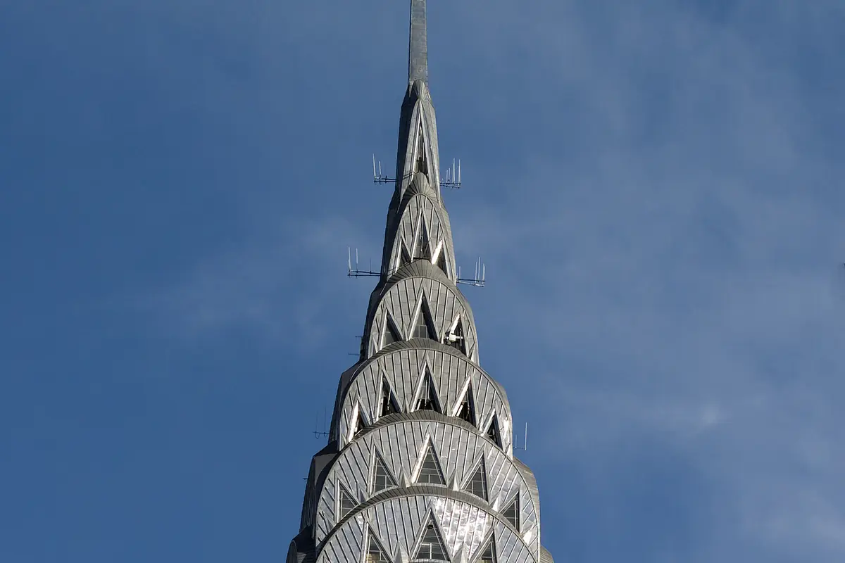 The Chrysler Building's stainless steel crown of stacked arches and triangular windows, rising to its spire against a blue sky